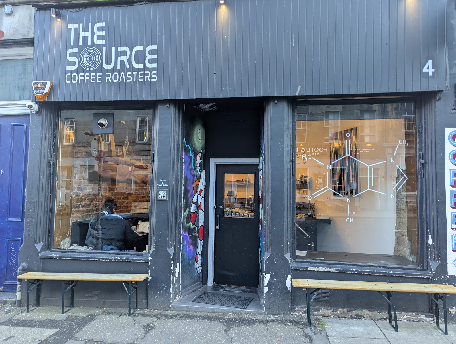 The dark front of the Source Coffee Roasters at 4 Spittal Street, with a caffeine molecule drawn on the window and benches along the pavement.