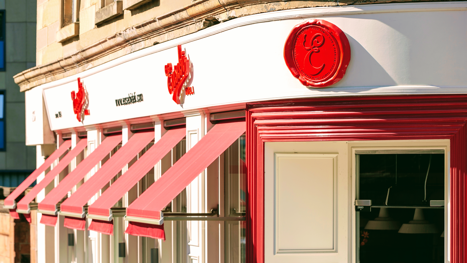 The corner front of Eusebi Deli on Park Road, with red awnings and the deli's red seal in the sun.