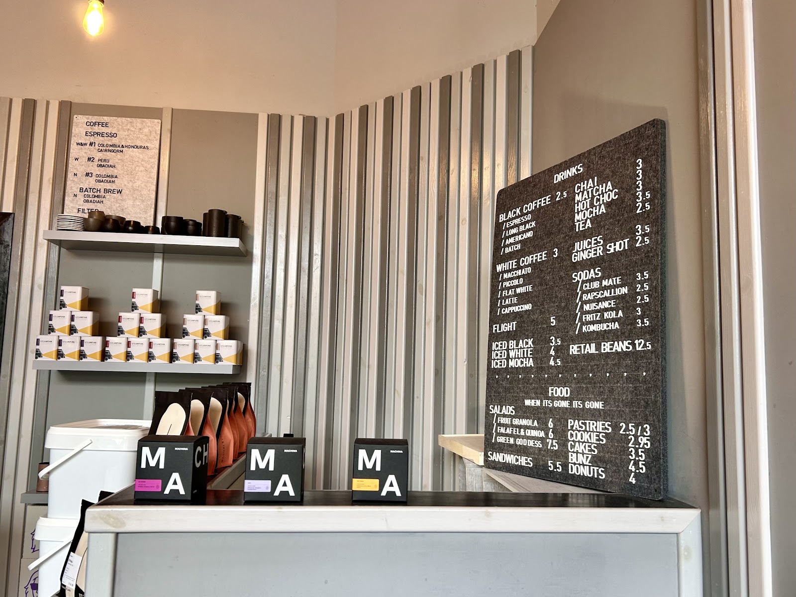 The counter at Little Fitzroy, with its drinks and food board, bags of coffee beans and shelves of cups behind.