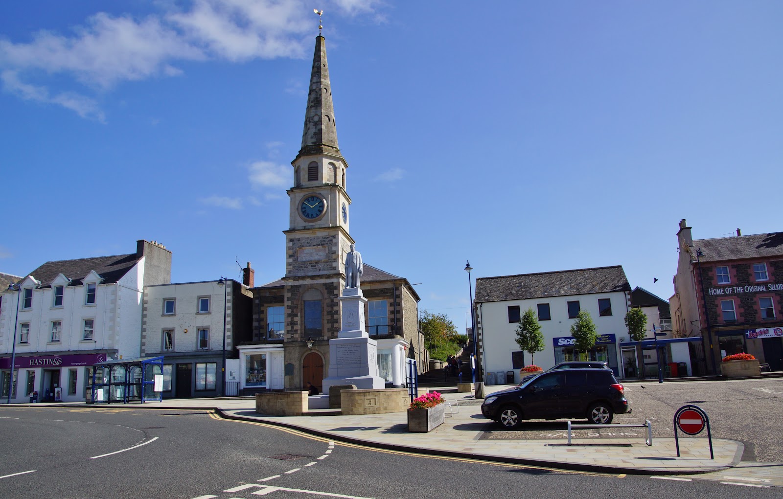 Sir Walter Scott's Courtroom on Selkirk's Market Place on a sunny day: the old town hall with its clock tower and tall spire, and Scott's statue on a plinth in front.