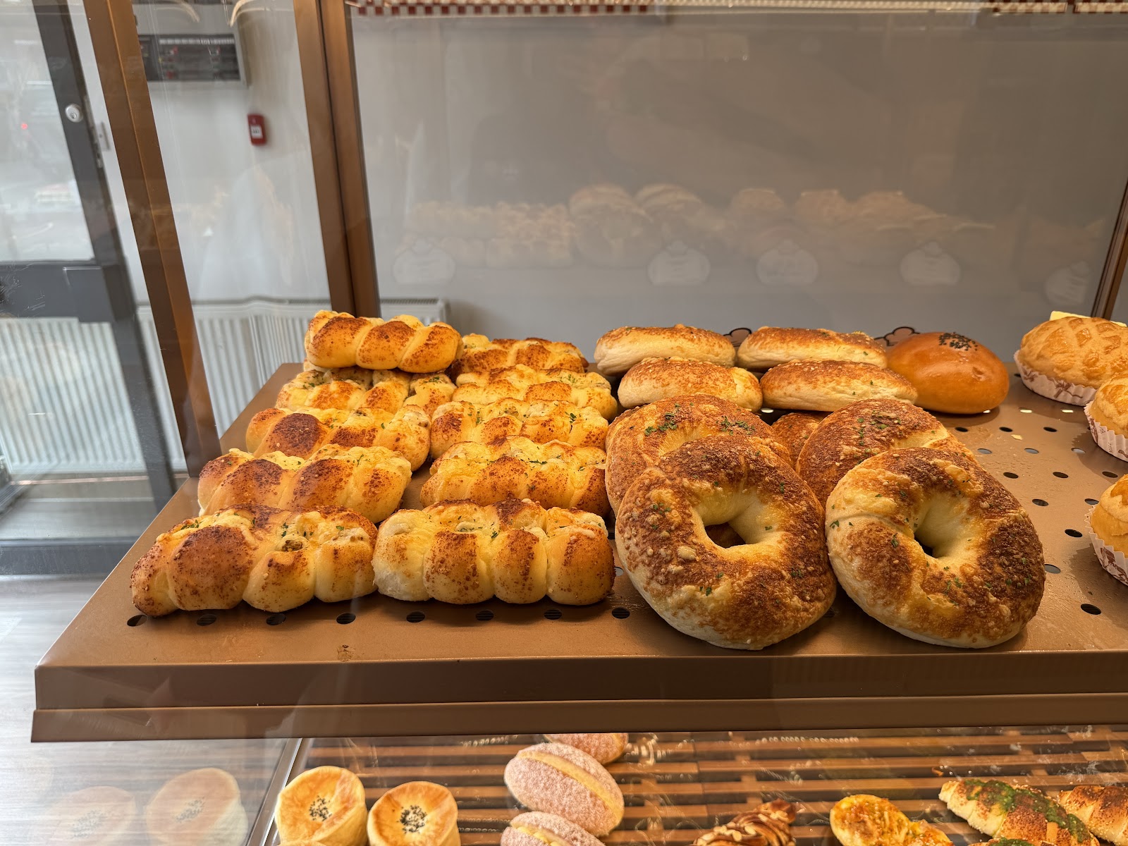 Plaited cheese buns and topped bagels on a copper tray behind the glass of the counter at Kungfu Bakery on Nicolson Square.