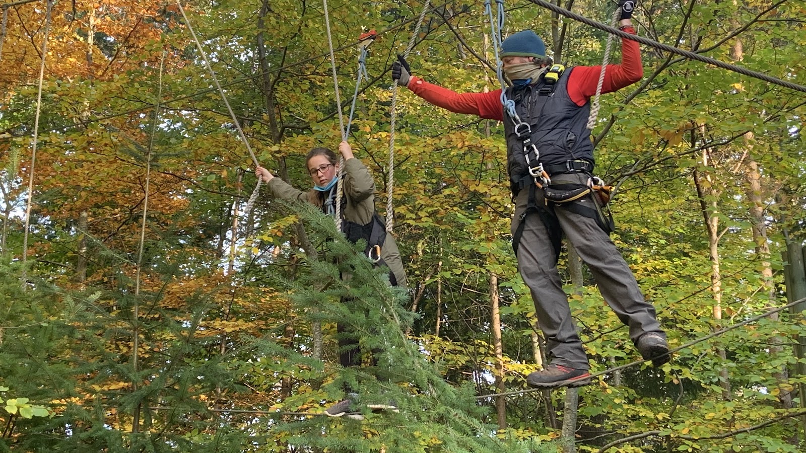 A climber crossing between platforms among autumn trees.