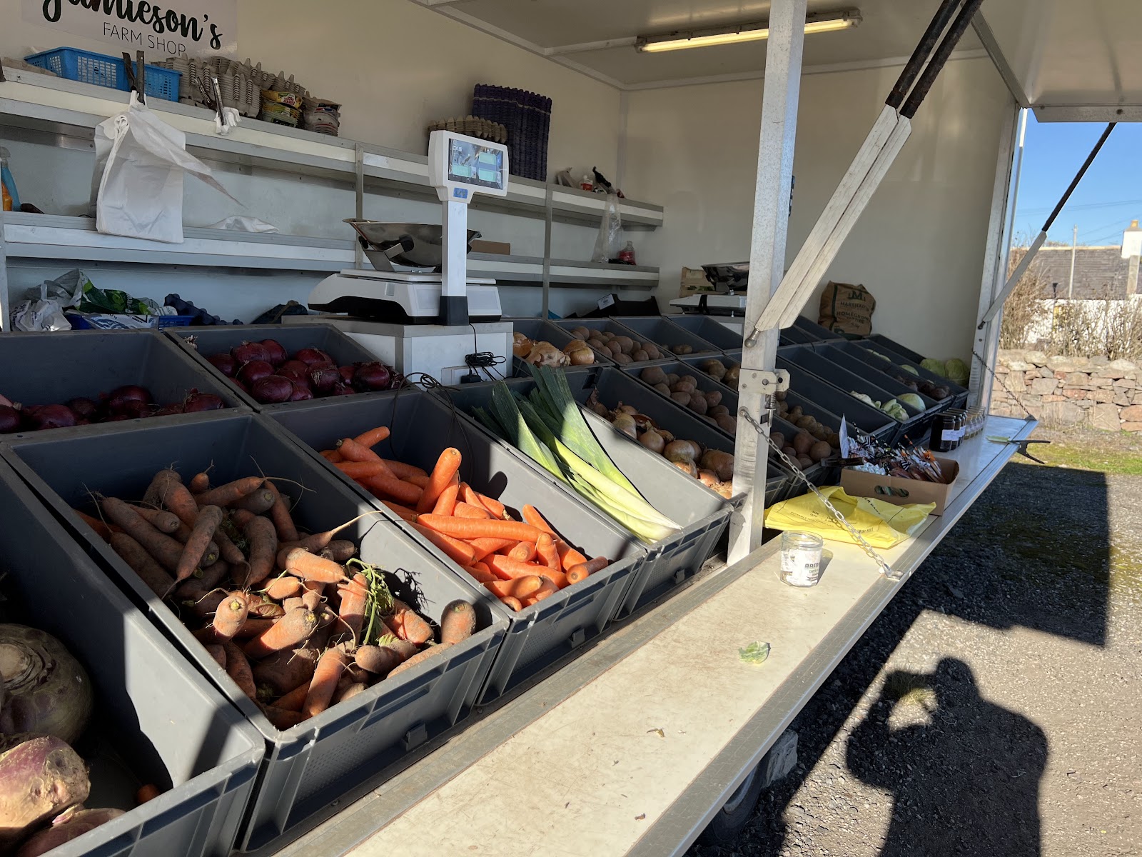 The counter at Jamieson's Farm Shop in Cove Bay, with crates of carrots, leeks, beetroot and potatoes in the sun.