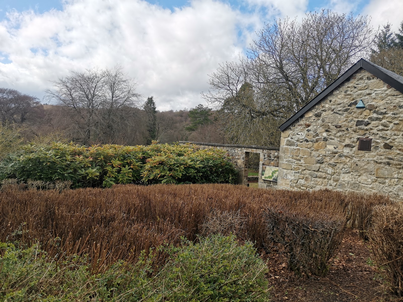 A stone farm building beside a hedged garden at Muiravonside, under a bright spring sky.