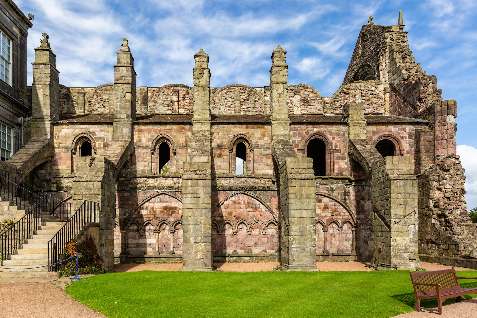 The ruined west front and arcaded wall of Holyrood Abbey against a blue sky.