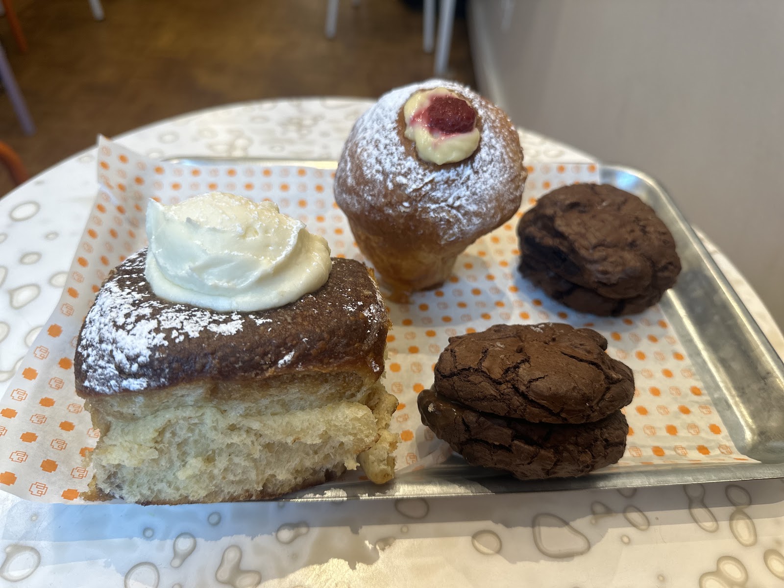 A tray of bakes at Burnfield Bakery on Pollokshaws Road: a cream-topped bun, a filled pastry and two chocolate cookies.