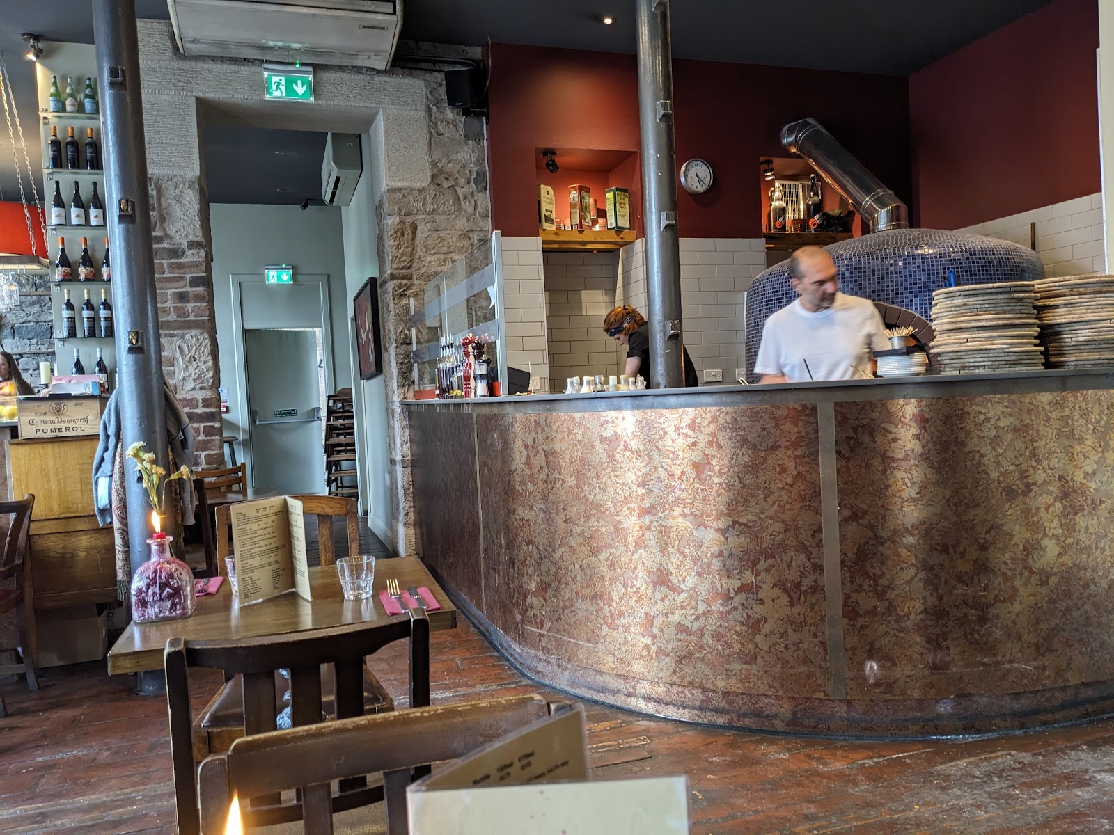 Origano's dining room on Leith Walk, with a copper-clad counter before the tiled pizza oven, bare stone walls and a candle on a wooden table.