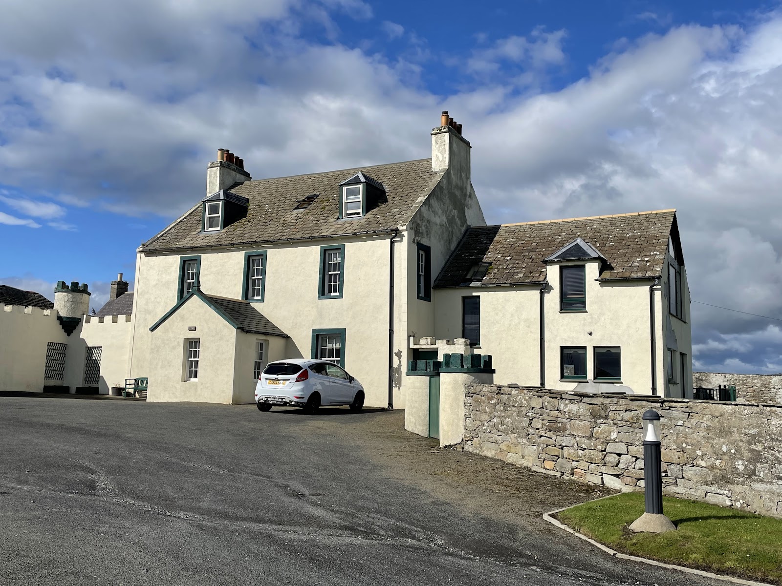 Pennyland House in Thurso, a white house of the 1700s with tall chimneys, under a blue sky.