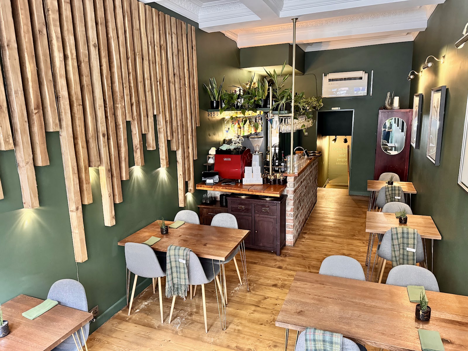 The narrow dining room at Dùthchas, with deep green walls, wooden tables, tartan throws on the chairs and a bar at the back.