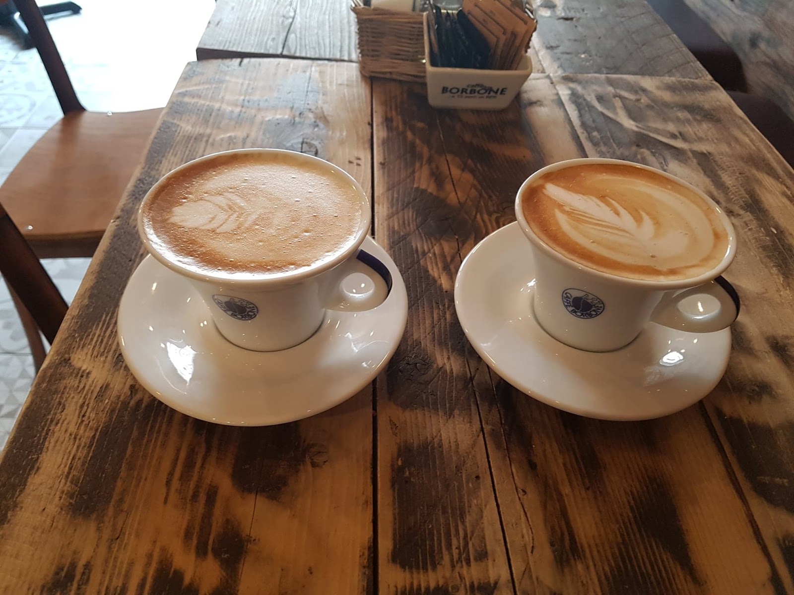 Two lattes with latte art on a rustic wooden table.