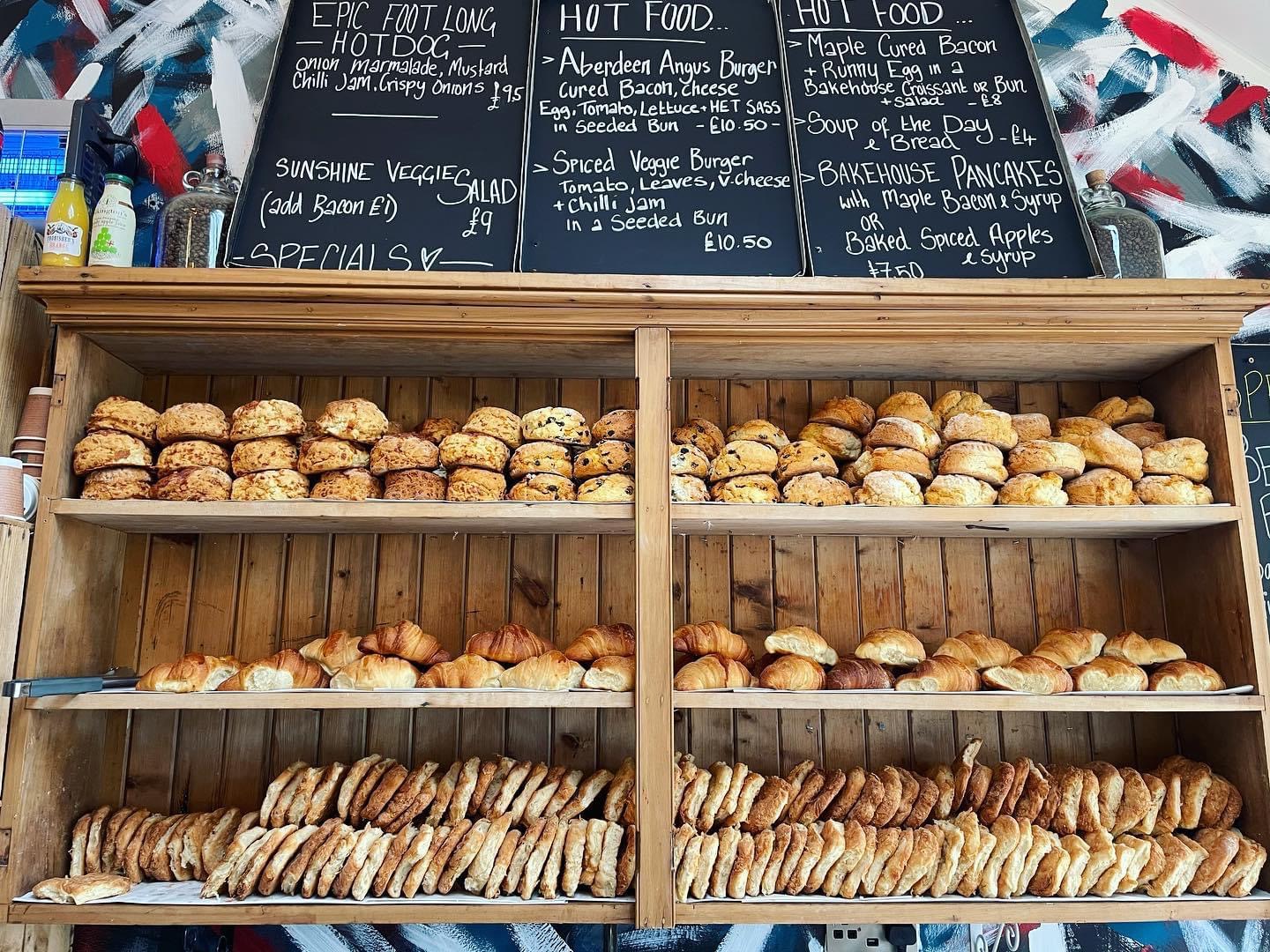 Shelves of fresh rolls, butteries and bakes at the Highlanders Bakehouse under a chalkboard.