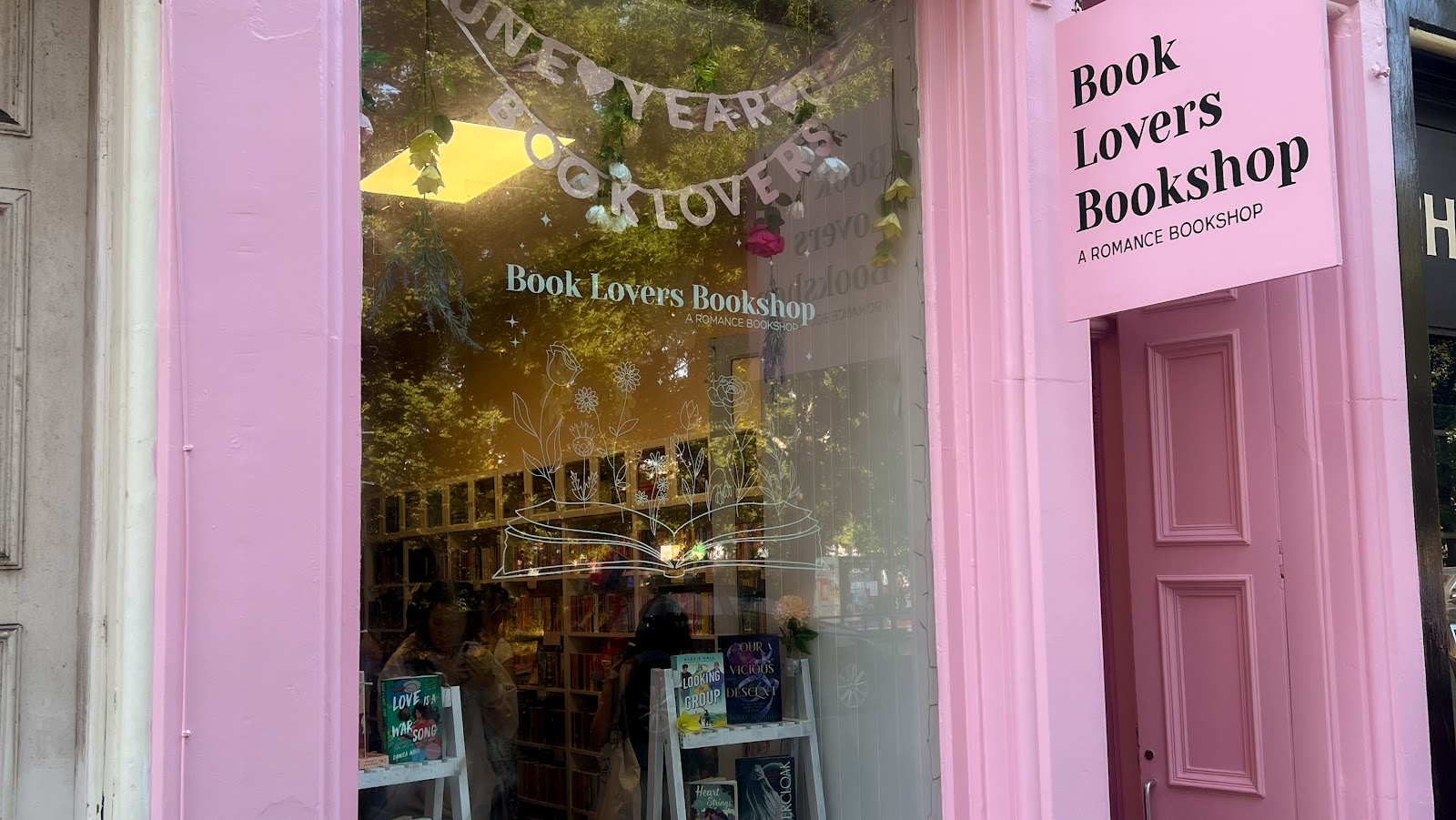 The pink front of Book Lovers Bookshop on Melville Terrace, its hanging sign reading A Romance Bookshop and romance novels in the window.