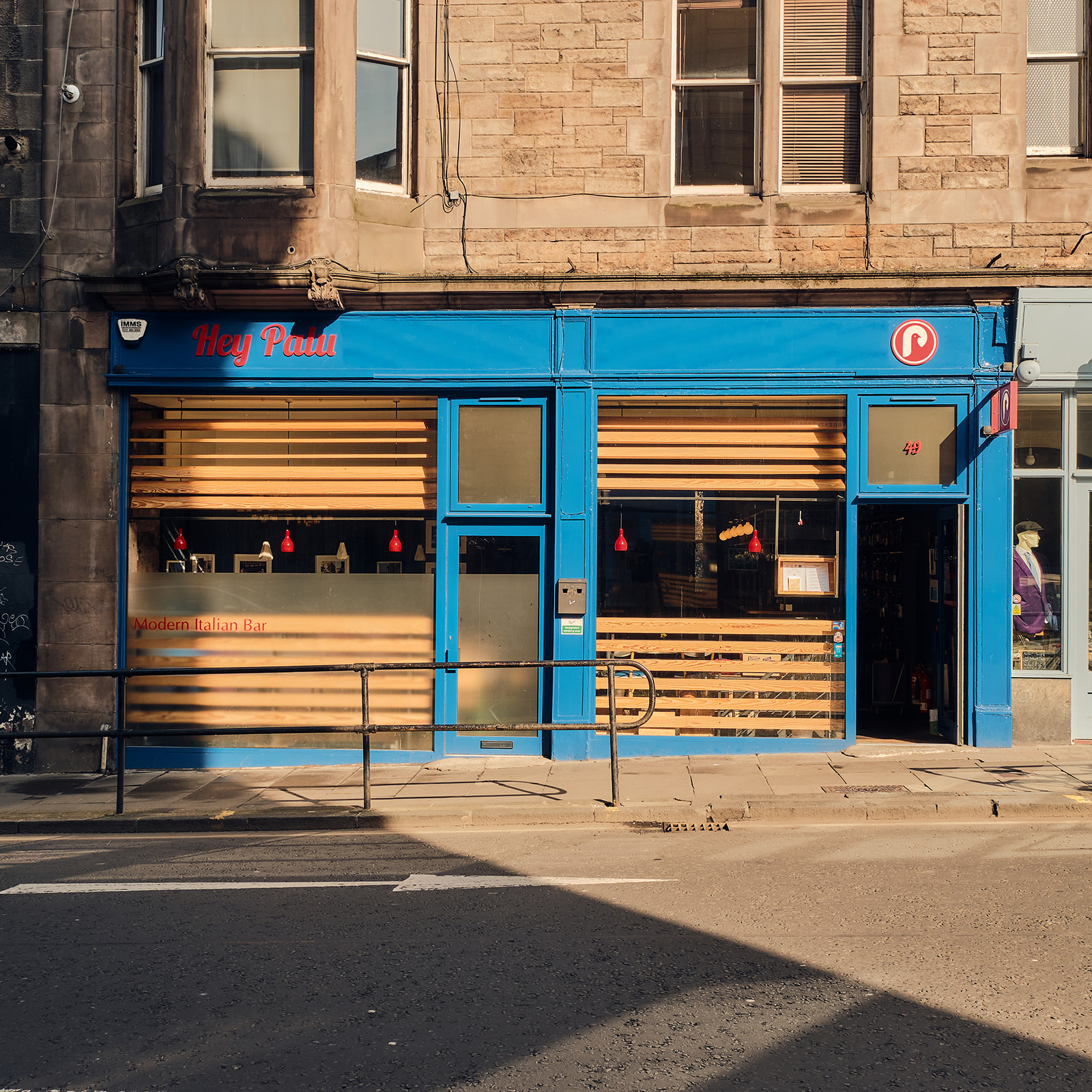 The blue front of Hey Palu on Bread Street in the sun, with its red sign, wooden slatted windows and the words Modern Italian Bar on the glass.