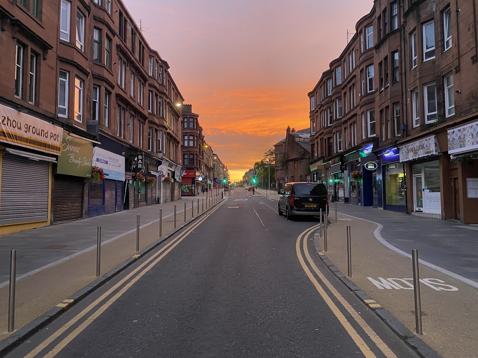 Byres Road at sunrise, empty of traffic, red sandstone tenements on both sides under an orange sky.