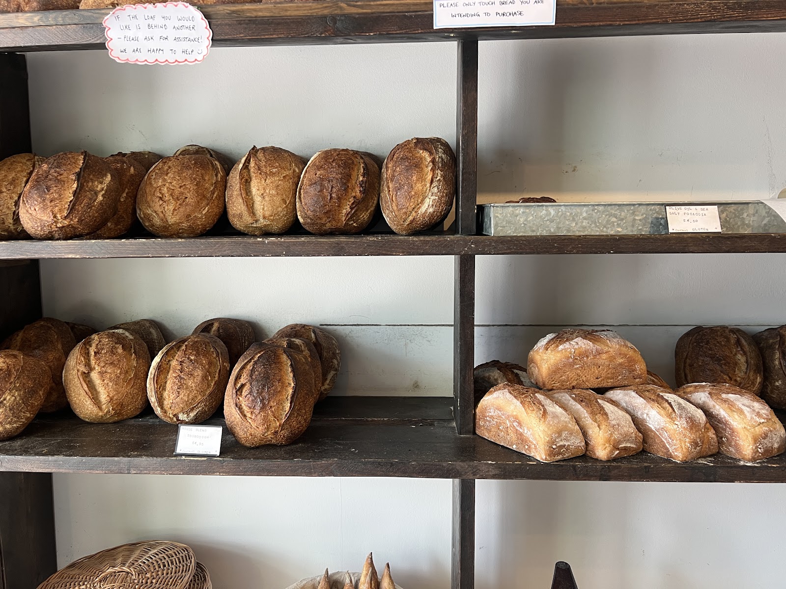Round sourdough loaves and floured tin loaves on dark wooden shelves against a white wall at Bandit Bakery on Rose Street.
