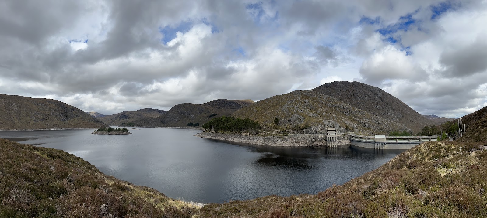Loch Monar at the head of Glen Strathfarrar, with a small island of pines, the curved Monar dam and its intake tower, and heather hills under broken cloud.