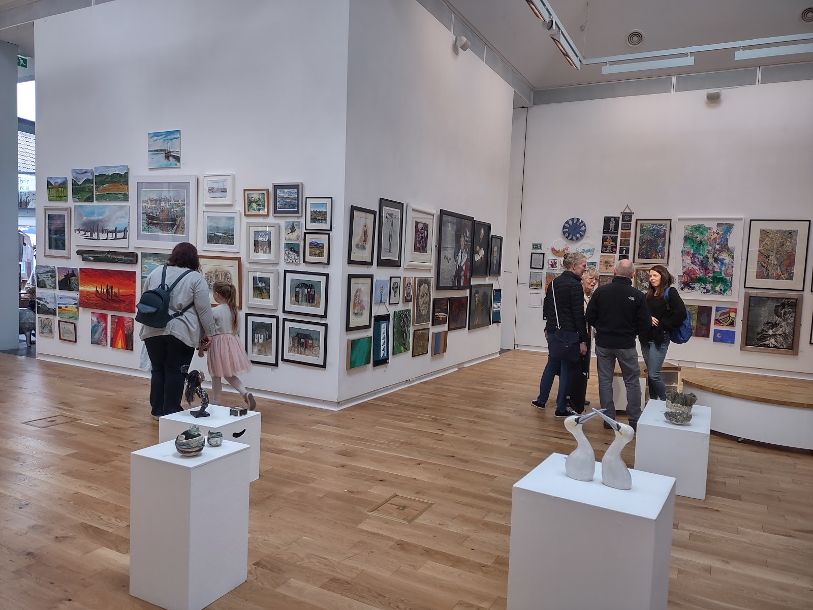 Visitors looking round an exhibition in An Lanntair's gallery, the white walls hung with paintings and prints, sculptures on plinths.