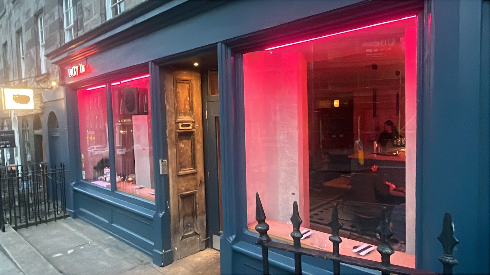 Lucky Yu's blue shopfront on Broughton Street at dusk, its windows lit pink by neon around an old wooden door.
