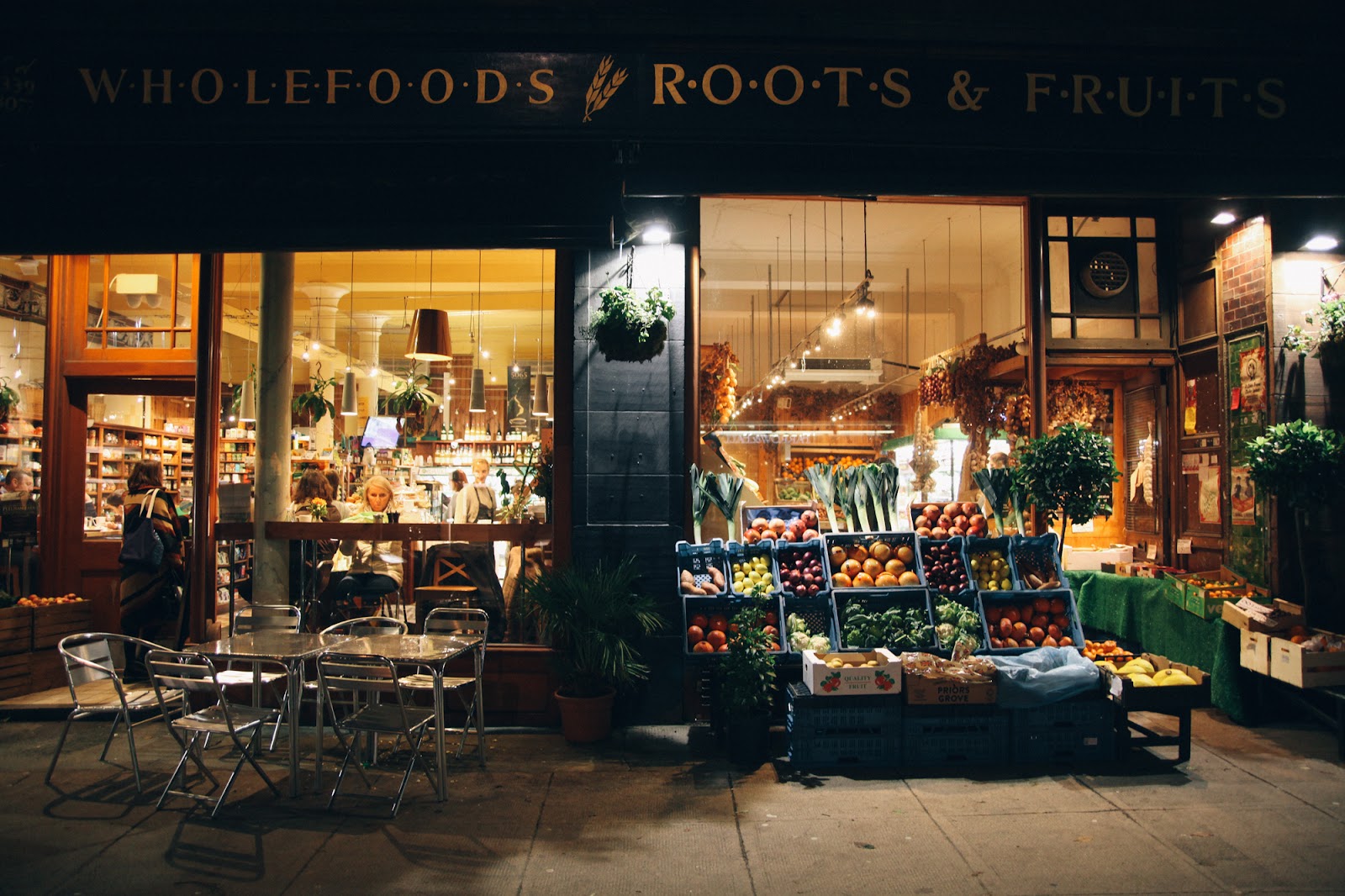 The shop lit at night, crates of fruit outside.