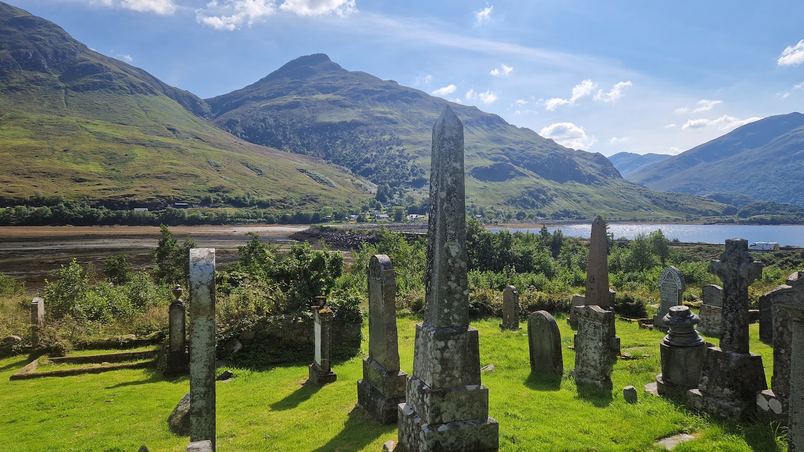 Old gravestones and a tall obelisk at Clachan Duich, the hills of Kintail and Loch Duich beyond.