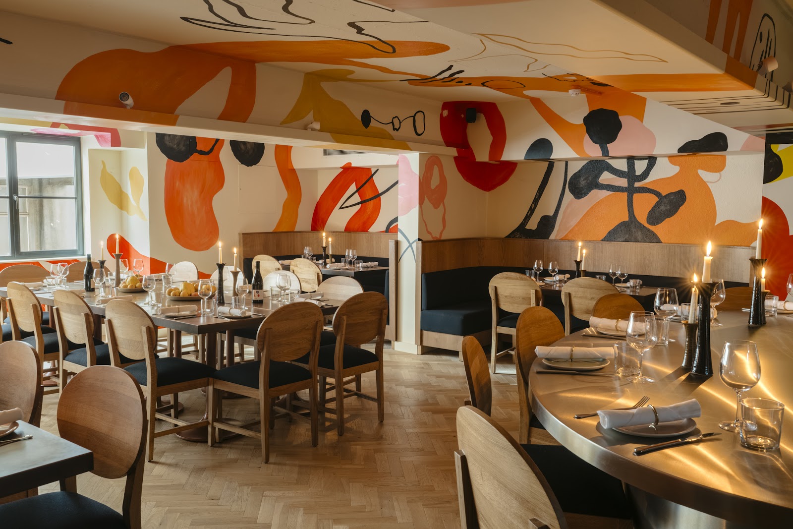 The dining room at Ottolenghi on George Street, wooden chairs and candlelit tables under walls painted with big orange, red and black shapes.