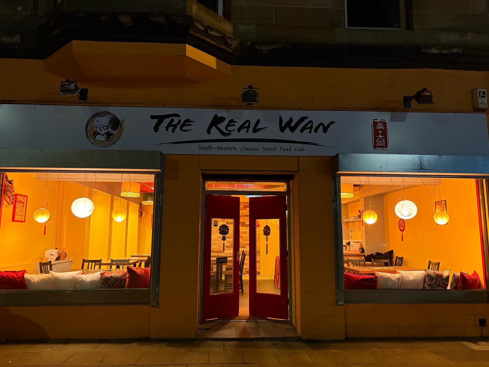 The Real Wan's orange front on Clincart Road at night, its red doors open and lanterns lit in the windows.
