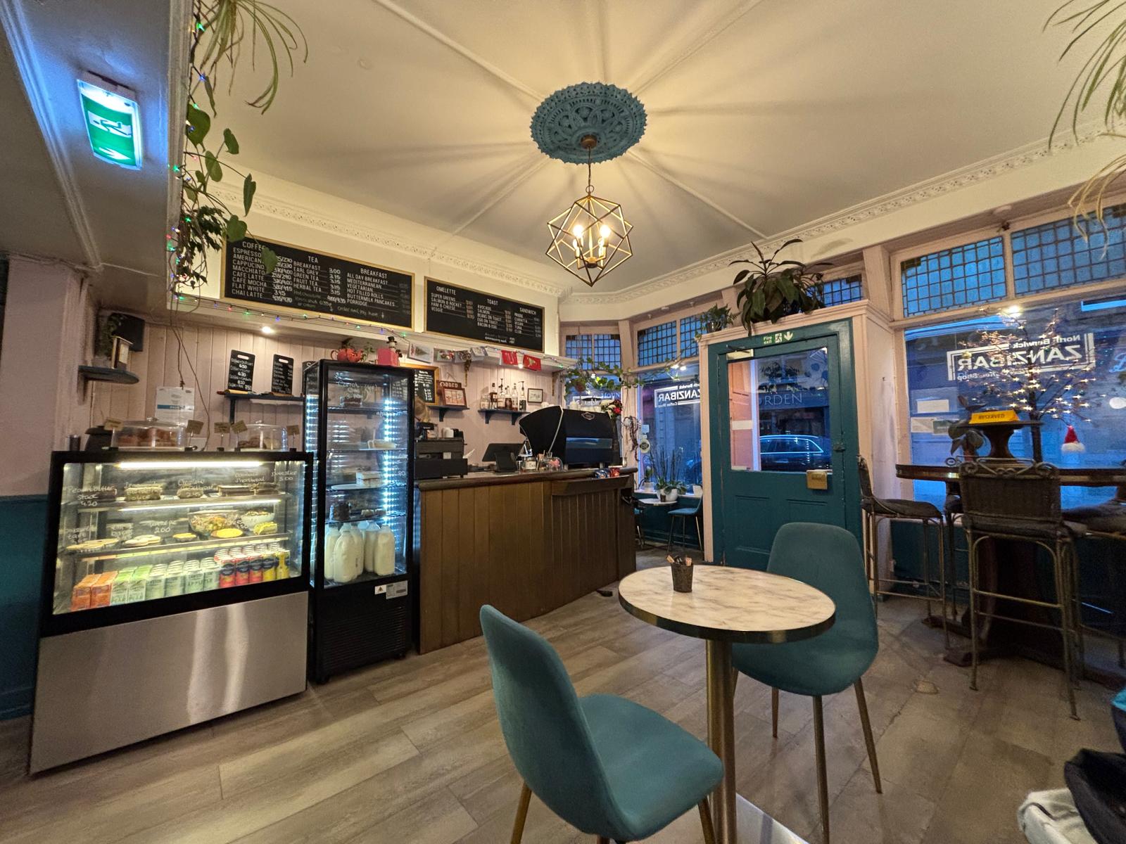 Inside Zanzibar Coffee Shop in North Berwick, teal chairs and a cake counter under a chalkboard menu.