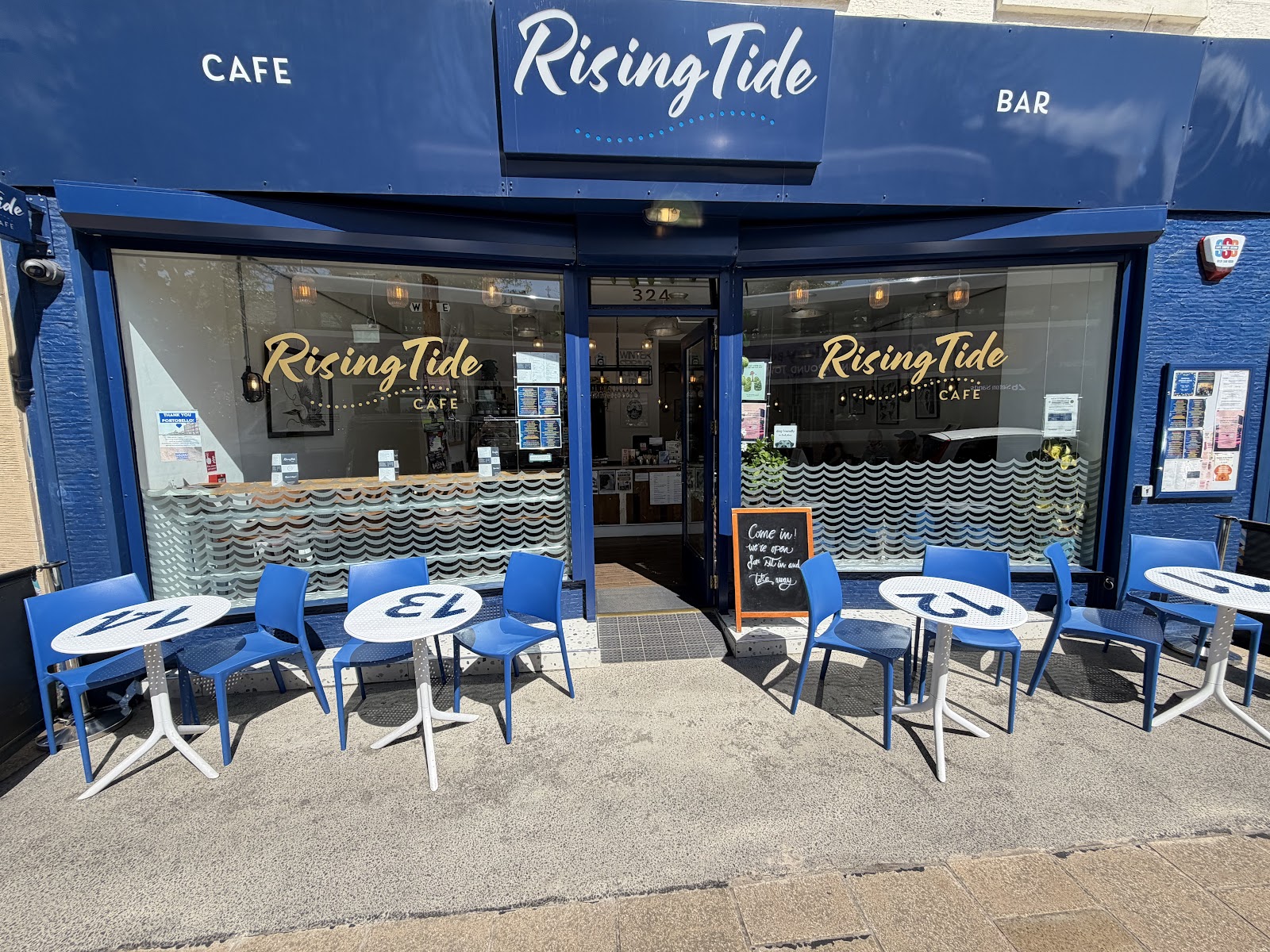 The blue shopfront of Rising Tide Cafe on Portobello High Street, with blue chairs and round tables out on the pavement.