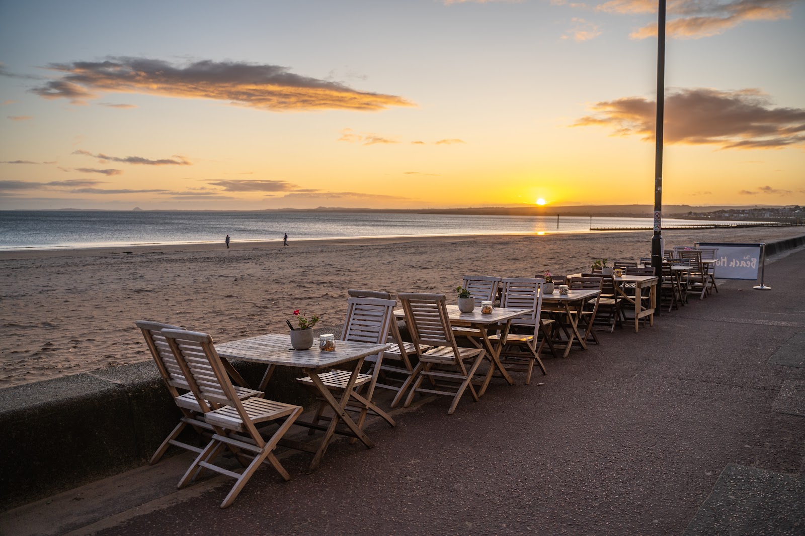 Tables of the Beach House on the promenade at Portobello, the sun setting over the sands.