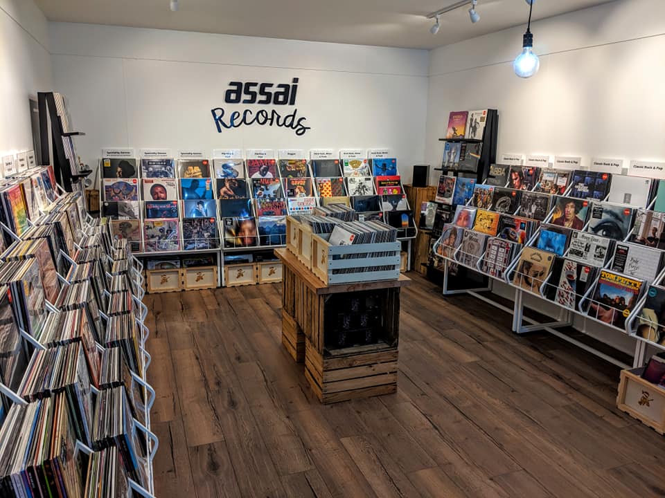 Inside Assai Records in Dundee: racks of vinyl round white walls under the shop's sign, with a crate of records on a wooden floor.