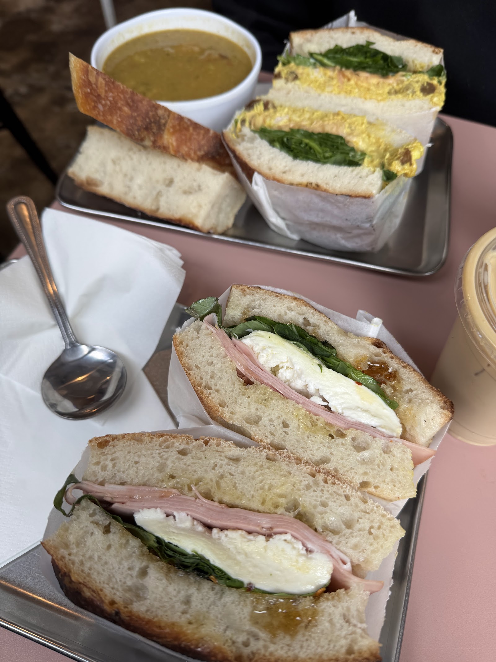 Two focaccia sandwiches, one of ham and mozzarella, with a bowl of soup on metal trays at Sister Midnight.