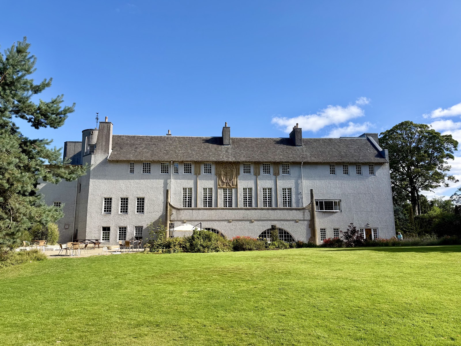 The white-harled House for an Art Lover behind a lawn and trees on a sunny day.