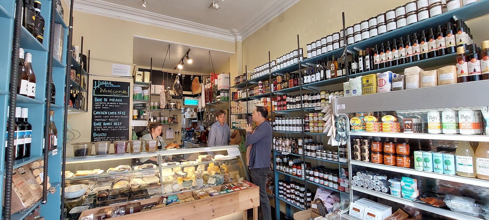 Inside Herbie of Edinburgh on Raeburn Place: the cheese counter, a chalkboard of the day's recommendations, hams hanging behind and shelves of jars, oils and wine.