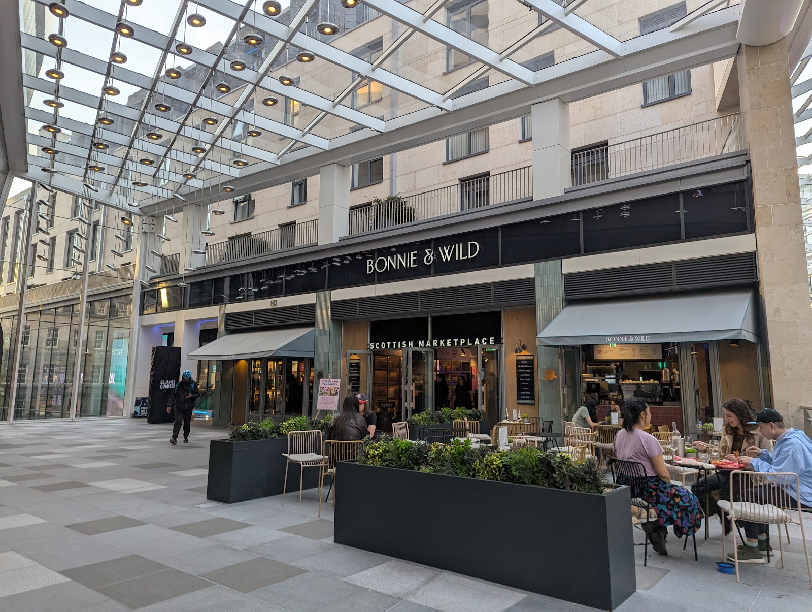 The front of Bonnie & Wild on Level 4 of the St James Quarter, its name above the doors, with people eating at the tables outside under the glass roof.