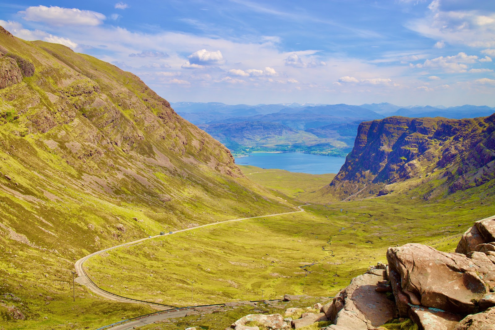 The single-track road of the Bealach na Ba winding up a green corrie, Loch Kishorn and distant hills below.