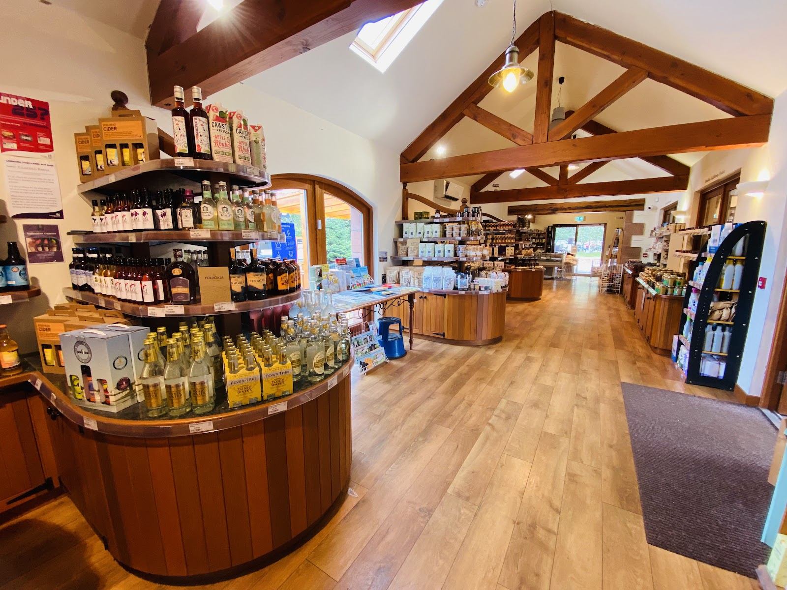 Inside Kilnford Farm Shop: timber roof beams, a round wooden stand of ciders, gins and tonics, and aisles of shelves on a wooden floor.