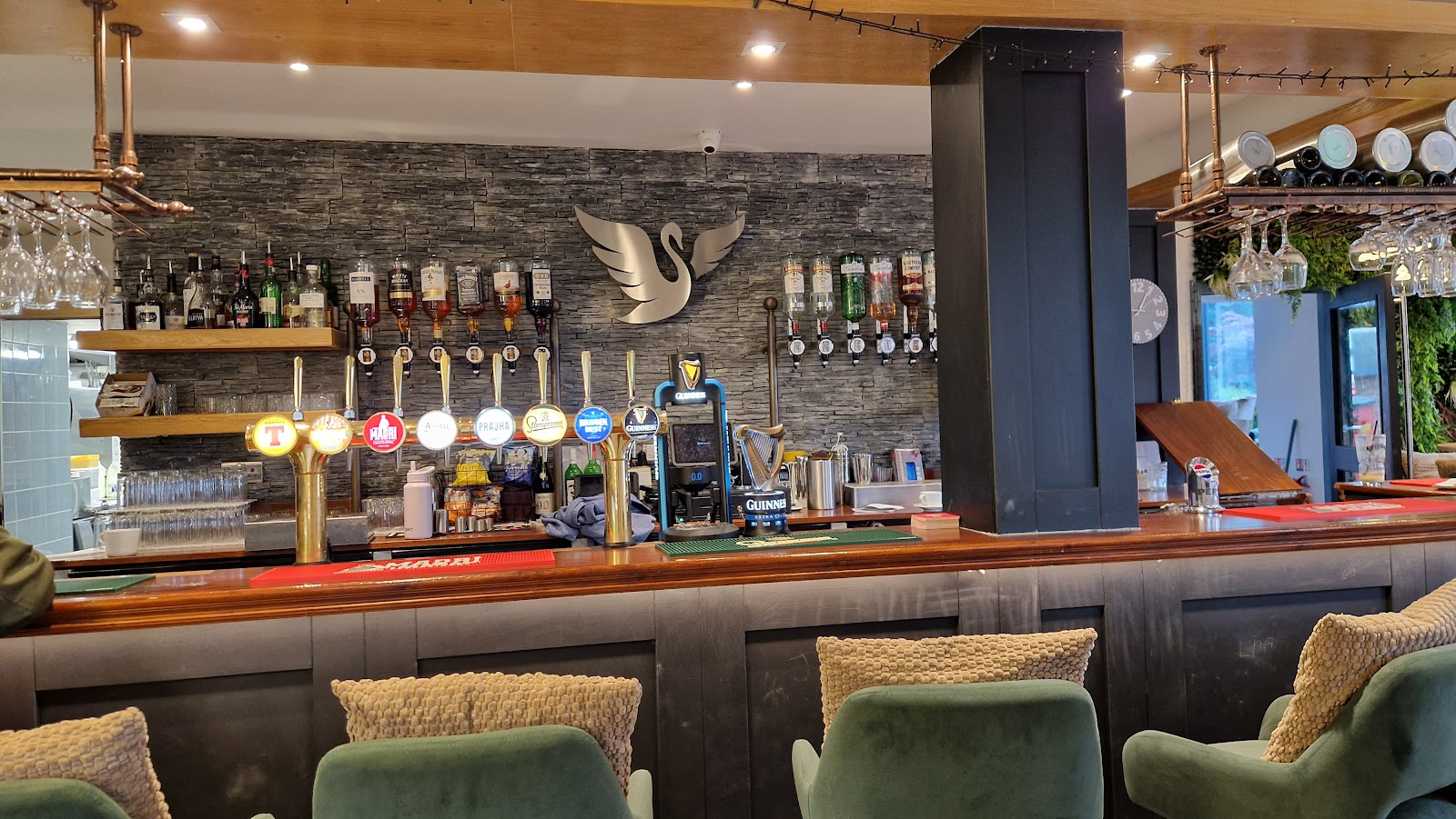 The bar at the Swan, a silver swan on a slate wall behind the taps, with green velvet stools in front.