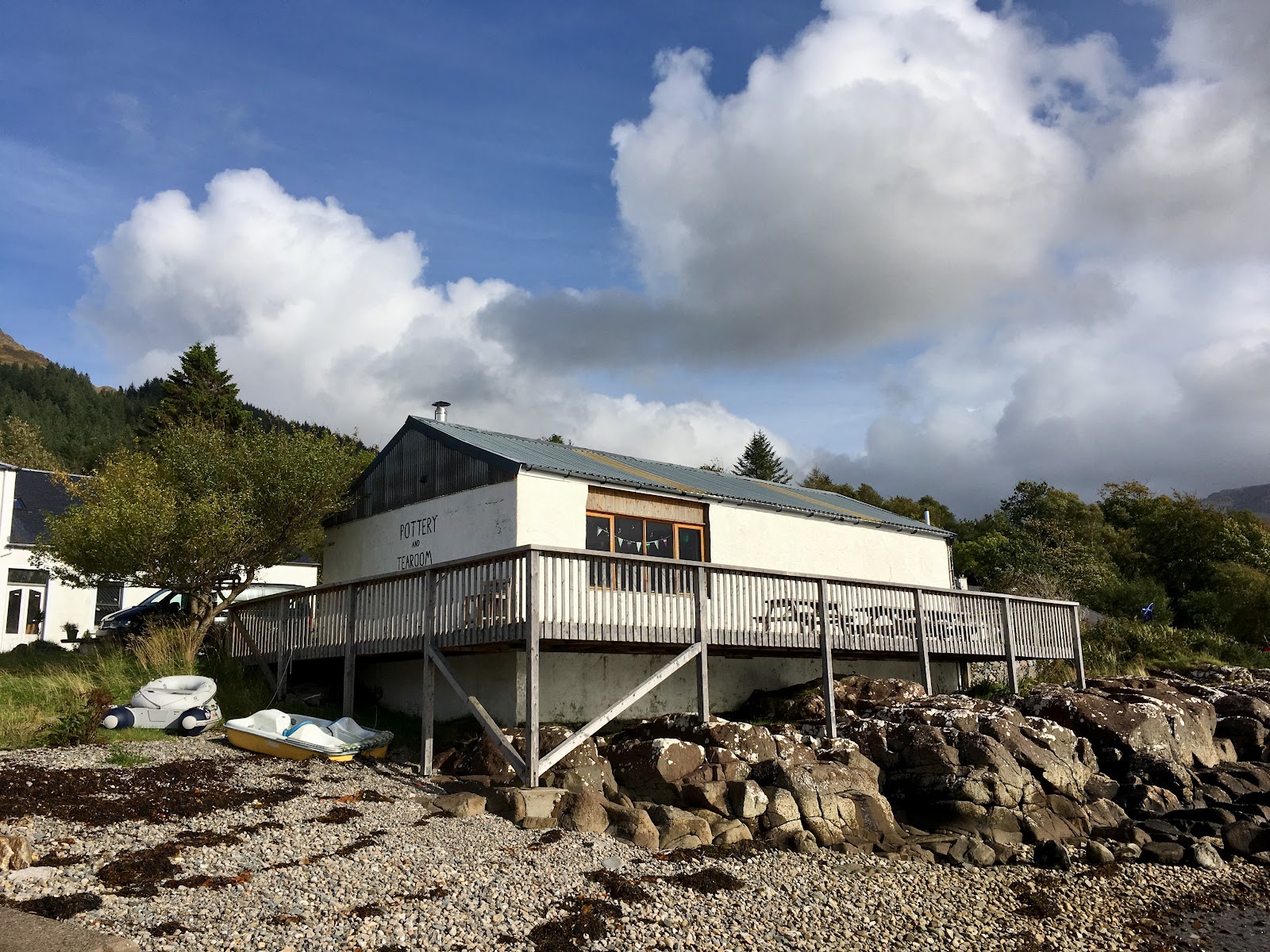 The Knoydart Pottery and Tea Room, a white timber building with a veranda on the rocky shore of Loch Nevis.