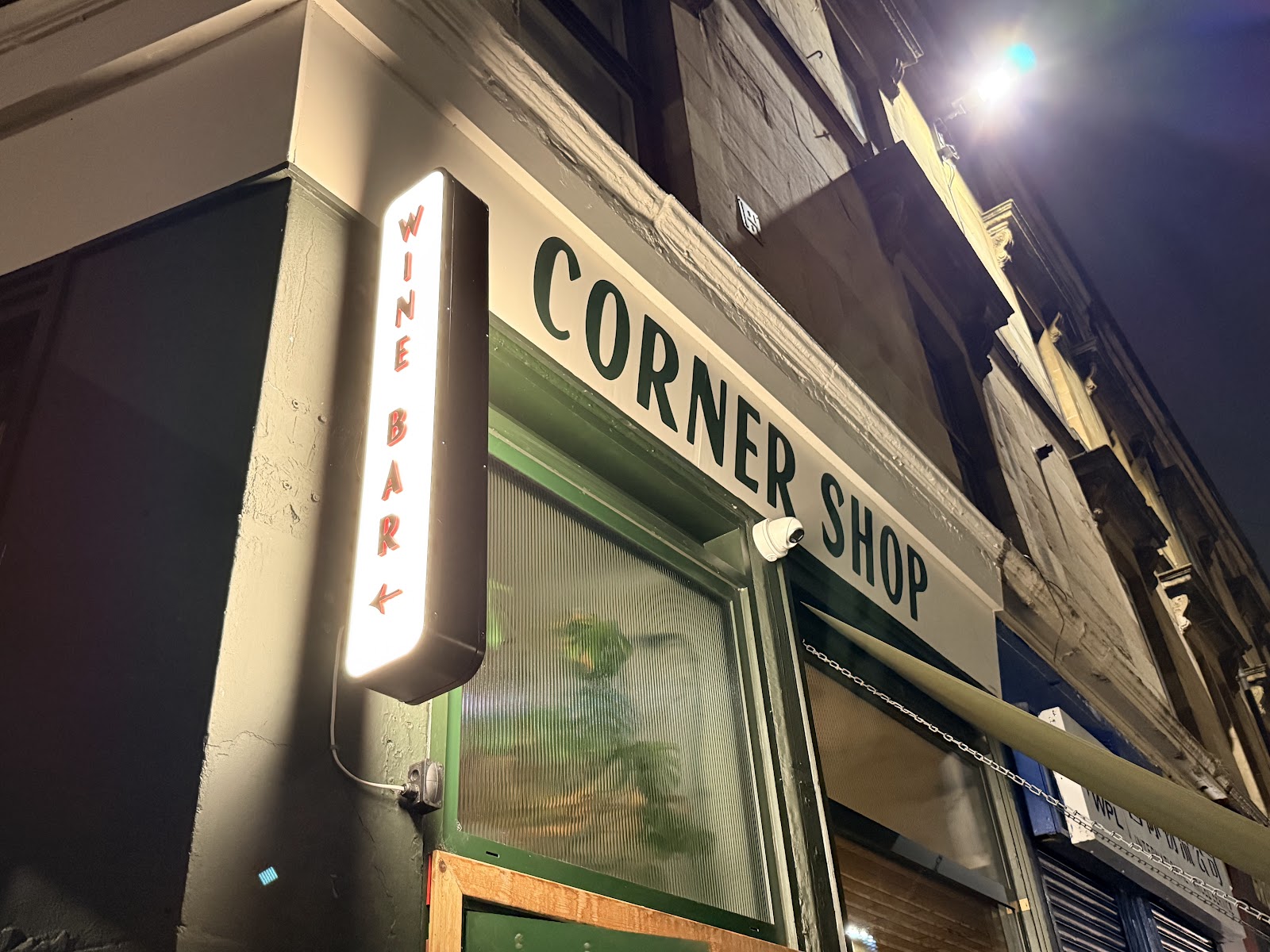The Corner Shop sign and its lit Wine Bar sign on the corner of Old Dumbarton Road at night.