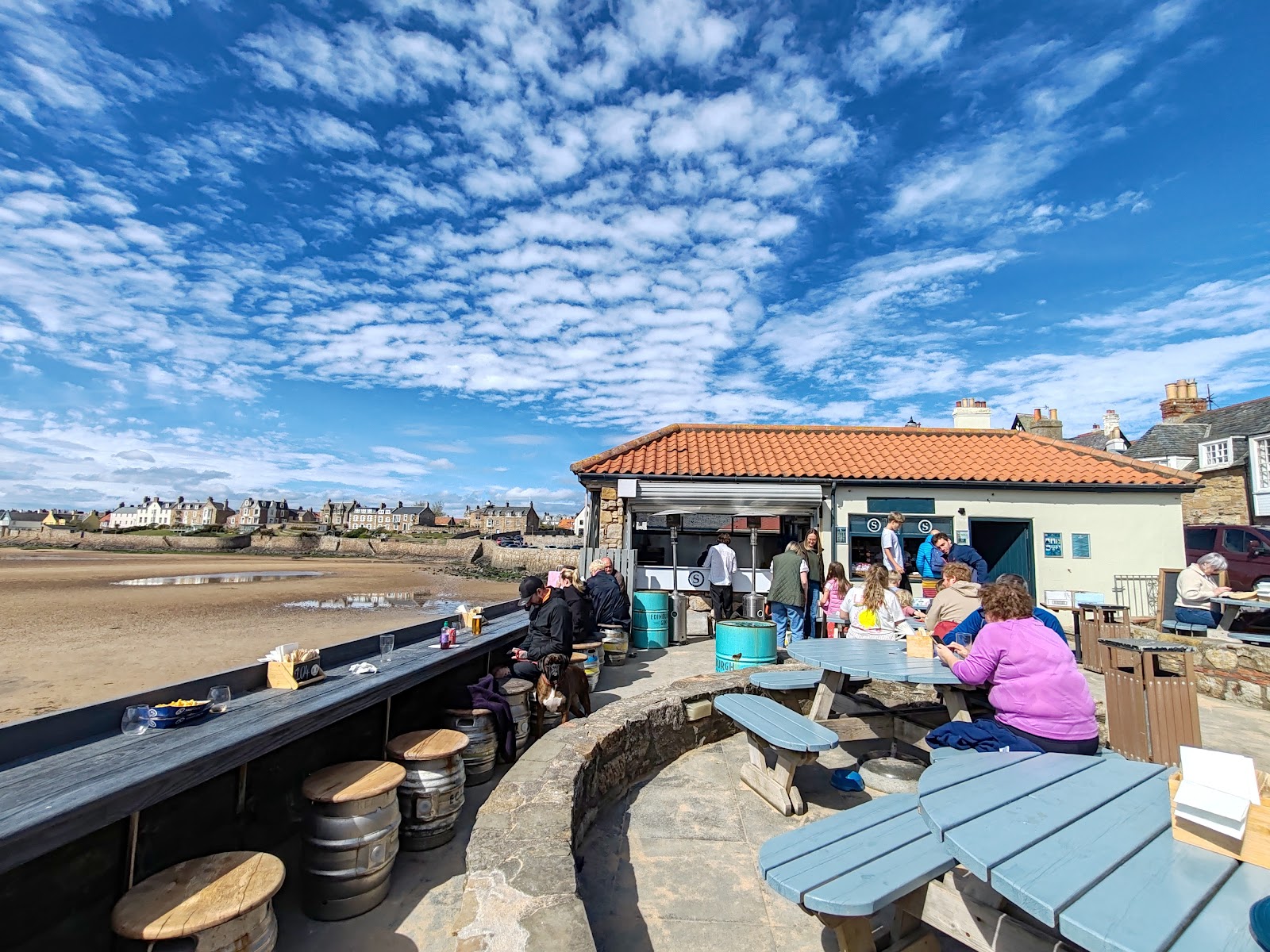The beach bar at the Ship Inn, tables and drinkers above the sands of Elie Bay under a blue sky.