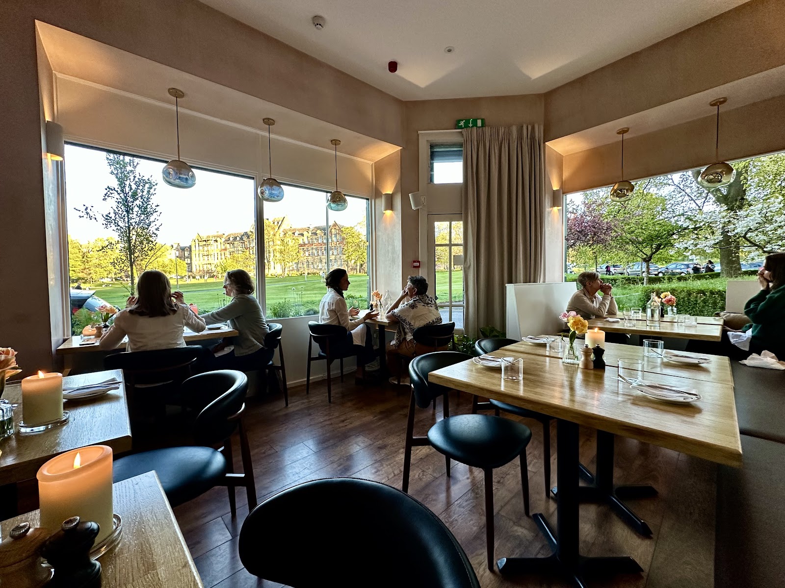Diners at Leftfield on a spring evening, at tables by big corner windows looking out over the green of Bruntsfield Links.