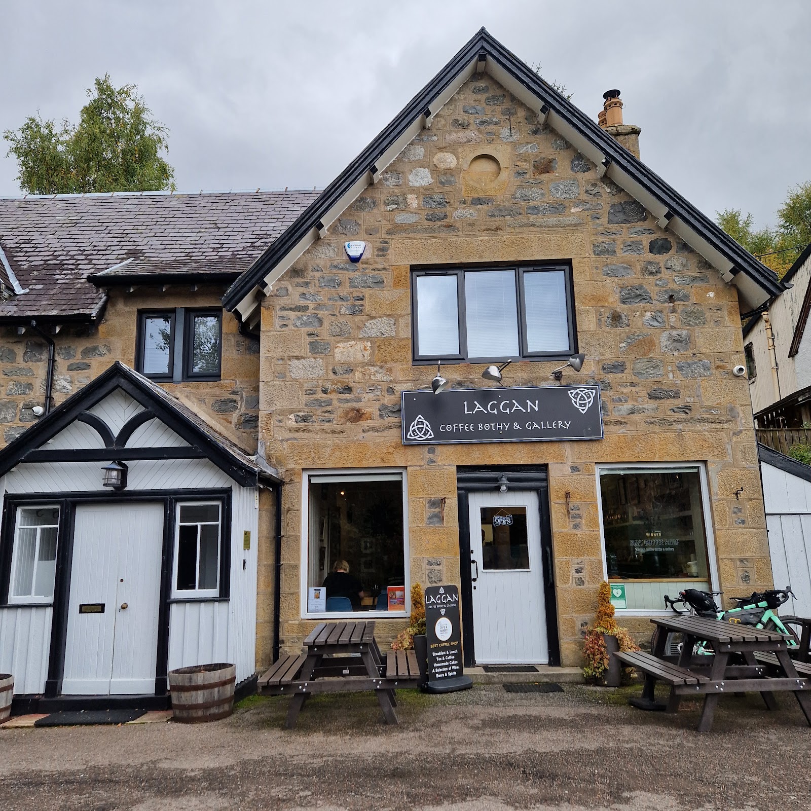 The stone front of Laggan Coffee Bothy and Gallery, with its sign over the door and picnic benches outside.