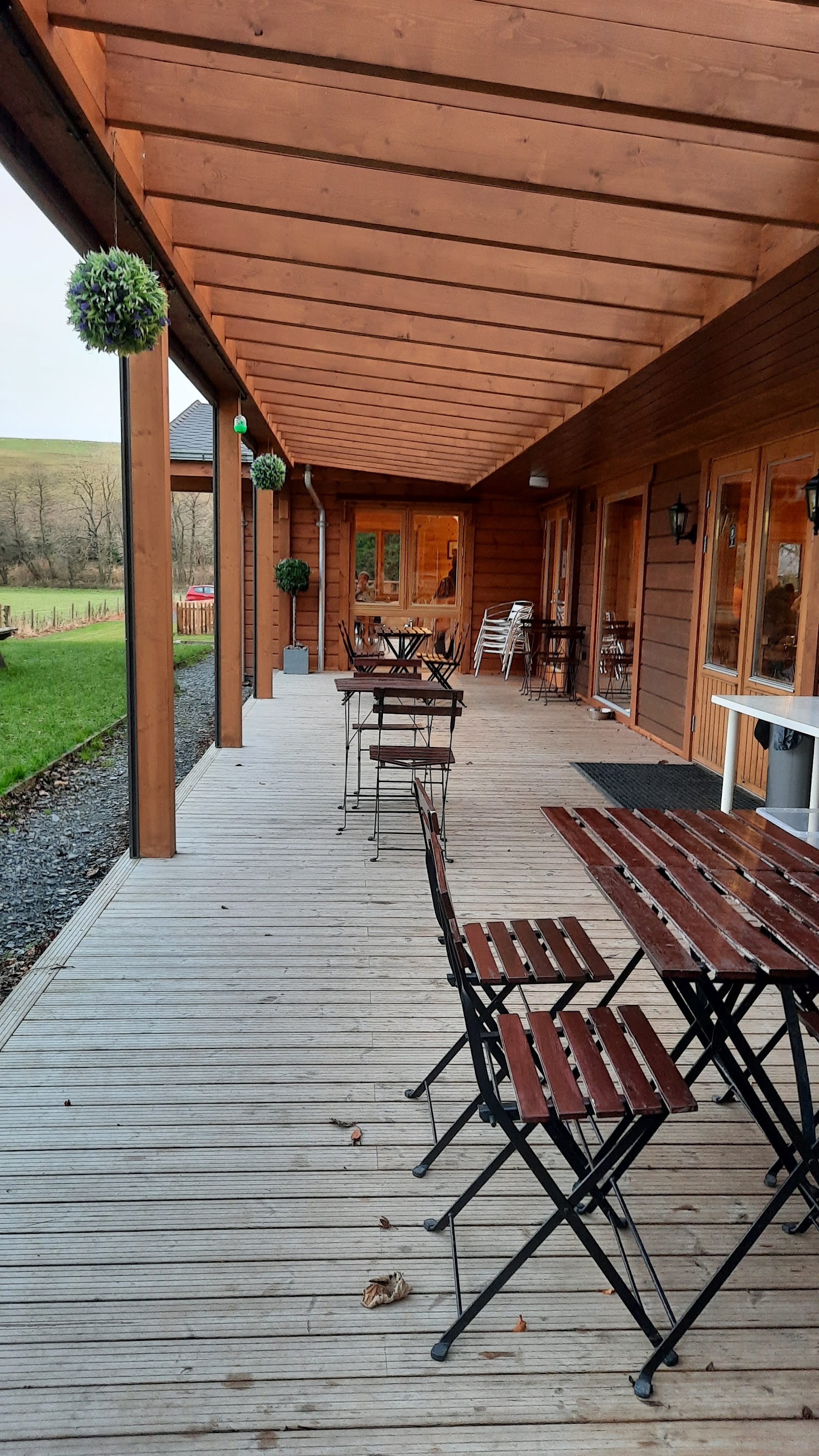 The Waterwheel Cafe's covered timber veranda at Philiphaugh, with folding tables and chairs along the deck and the cafe's glazed doors on the right.