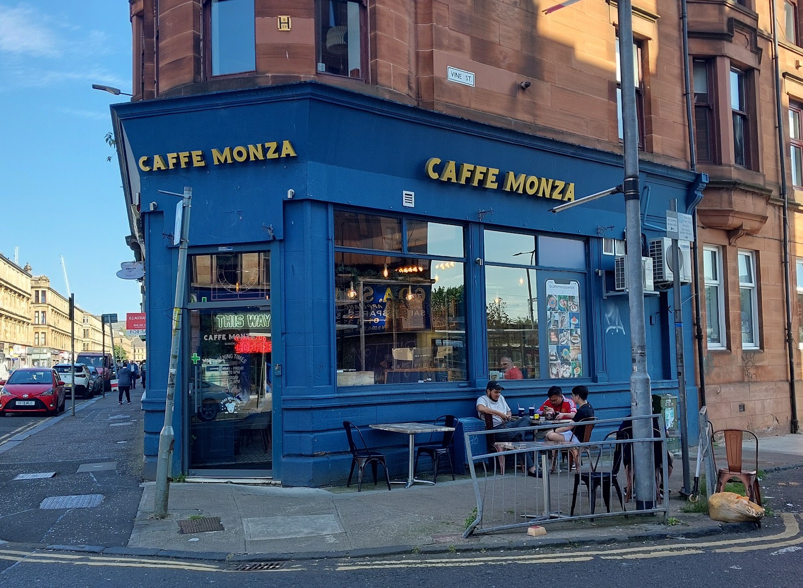 Caffe Monza's blue corner front on Dumbarton Road with tables outside.