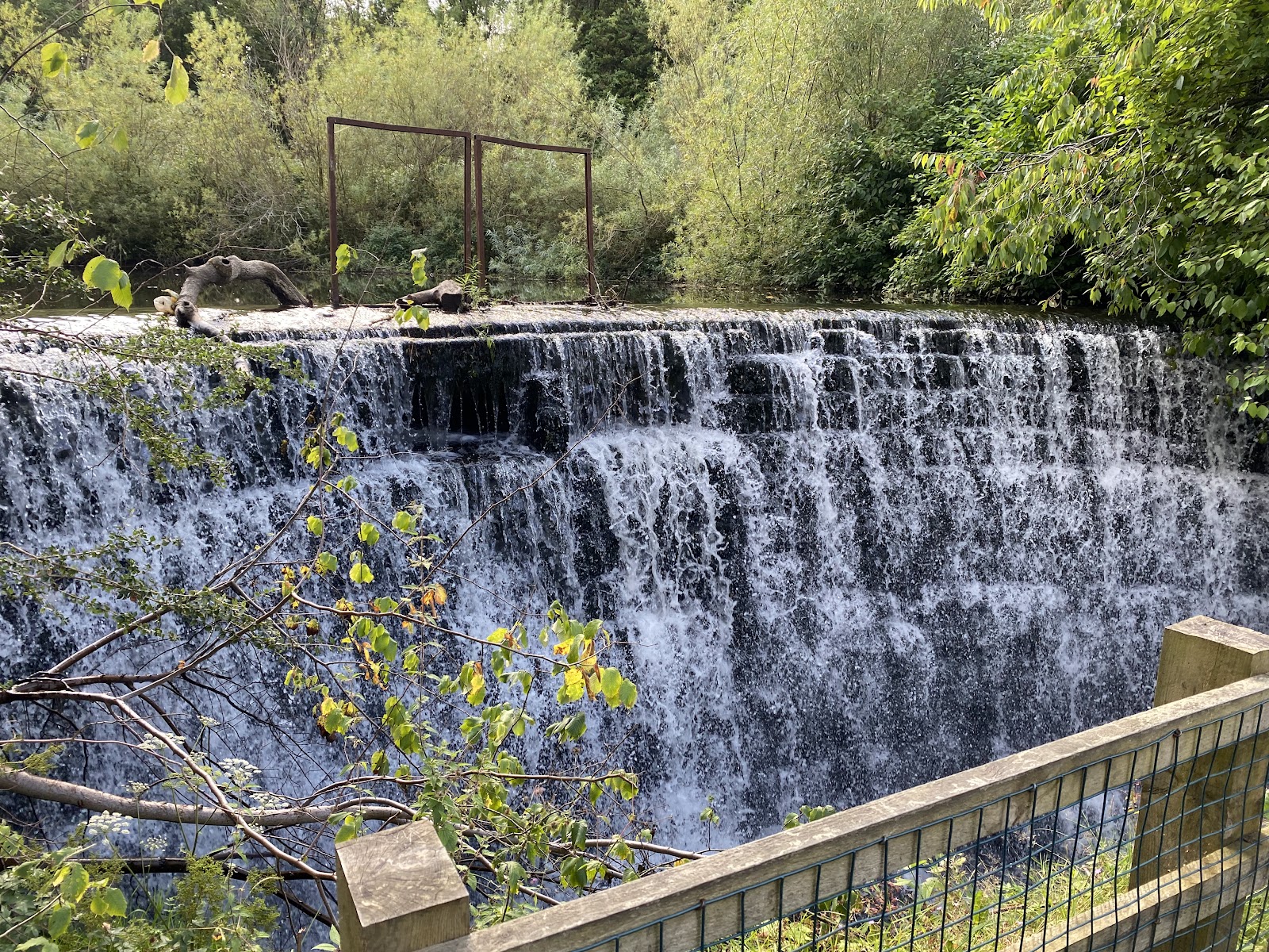 The broad curtain of the main waterfall in Rouken Glen pouring over its stone lip, seen from a fenced path.