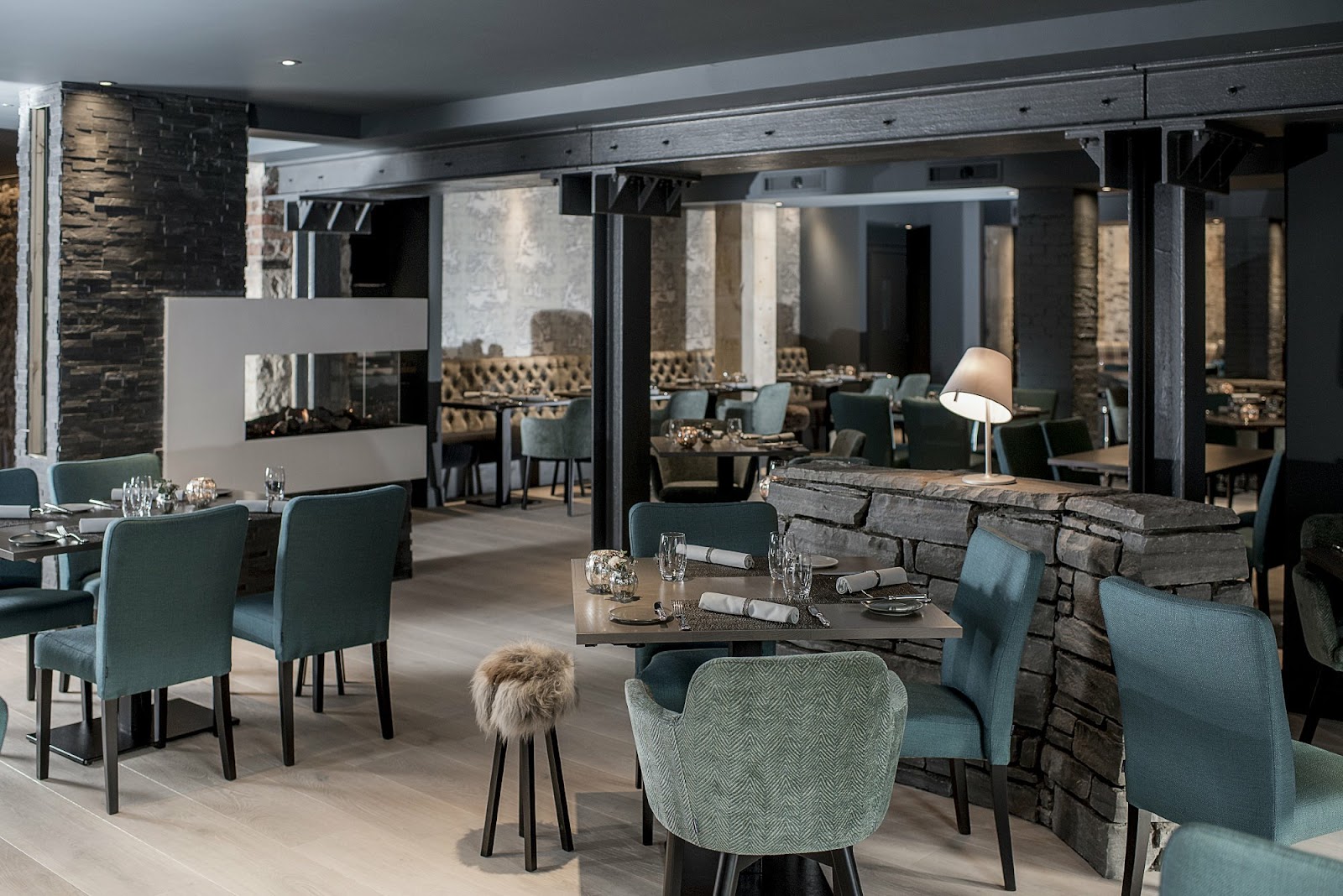 The dining room at The Kitchin, with grey stone walls, dark beams and blue-green chairs at tables laid for dinner.
