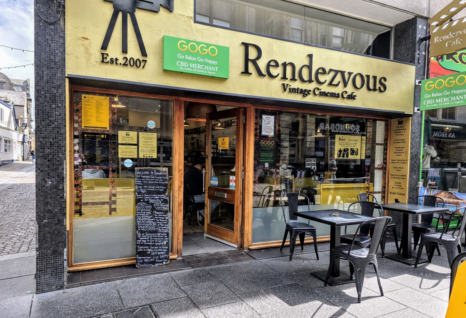 The yellow front of the Rendezvous Vintage Cinema Cafe on Church Street, Est. 2007, with tables and chairs outside.