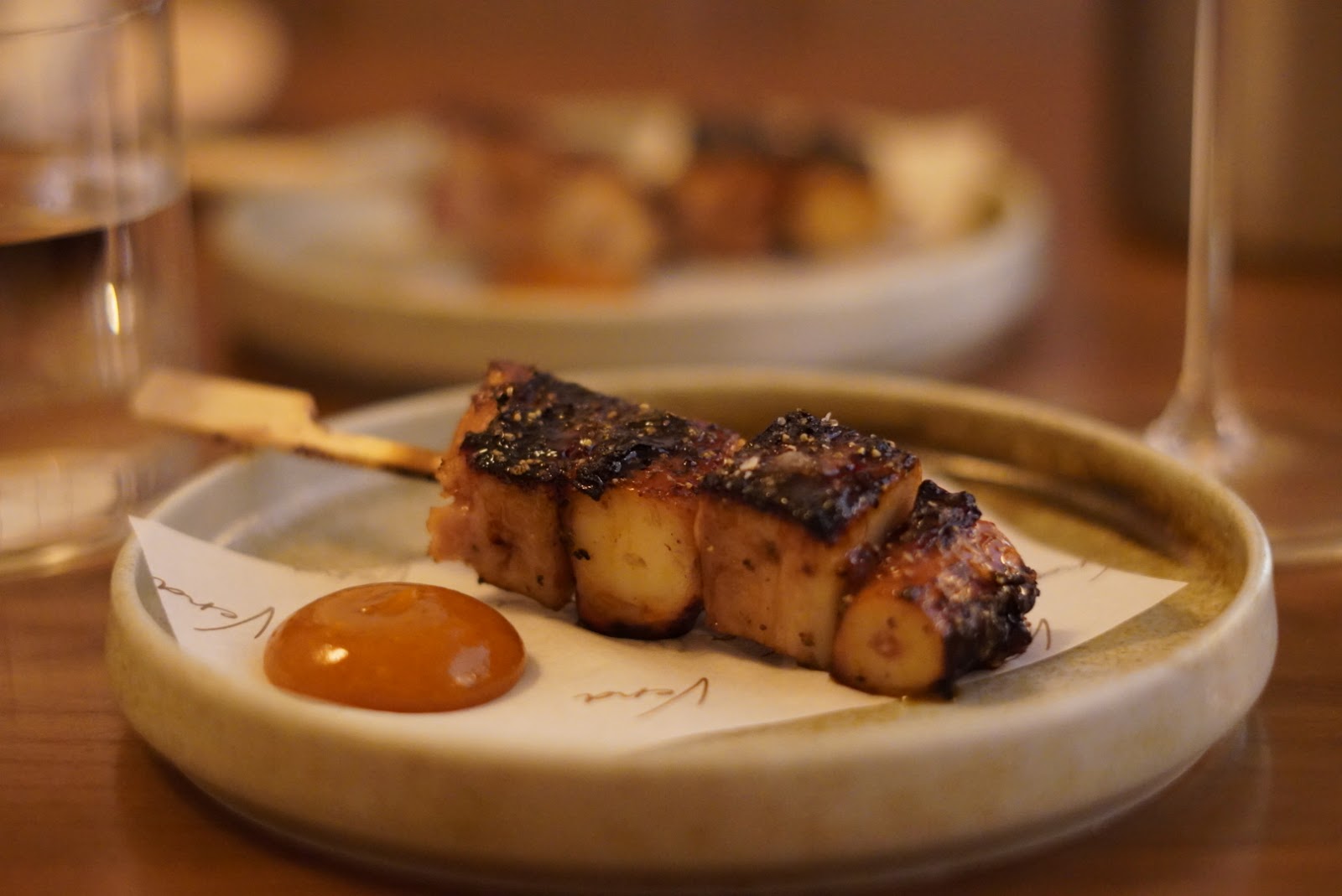 An octopus and pork skewer with kumquat hot sauce, on paper printed with the name Vera.
