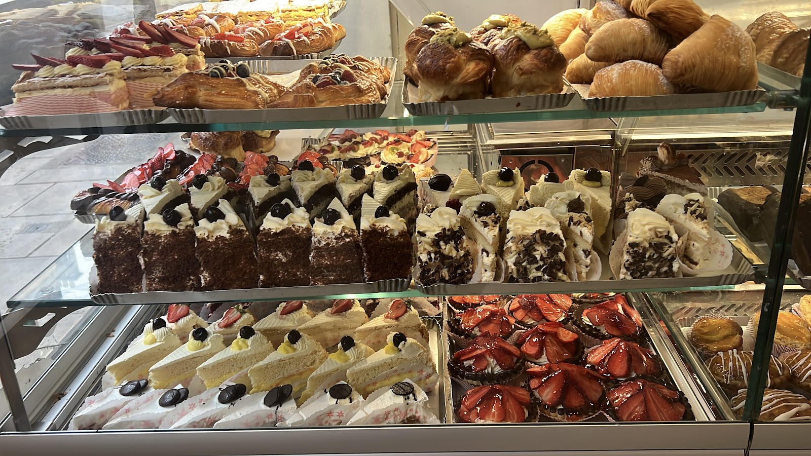 The glass counter full of cakes and pastries: strawberry tarts, cream sponge slices, chocolate gateau slices and croissants.
