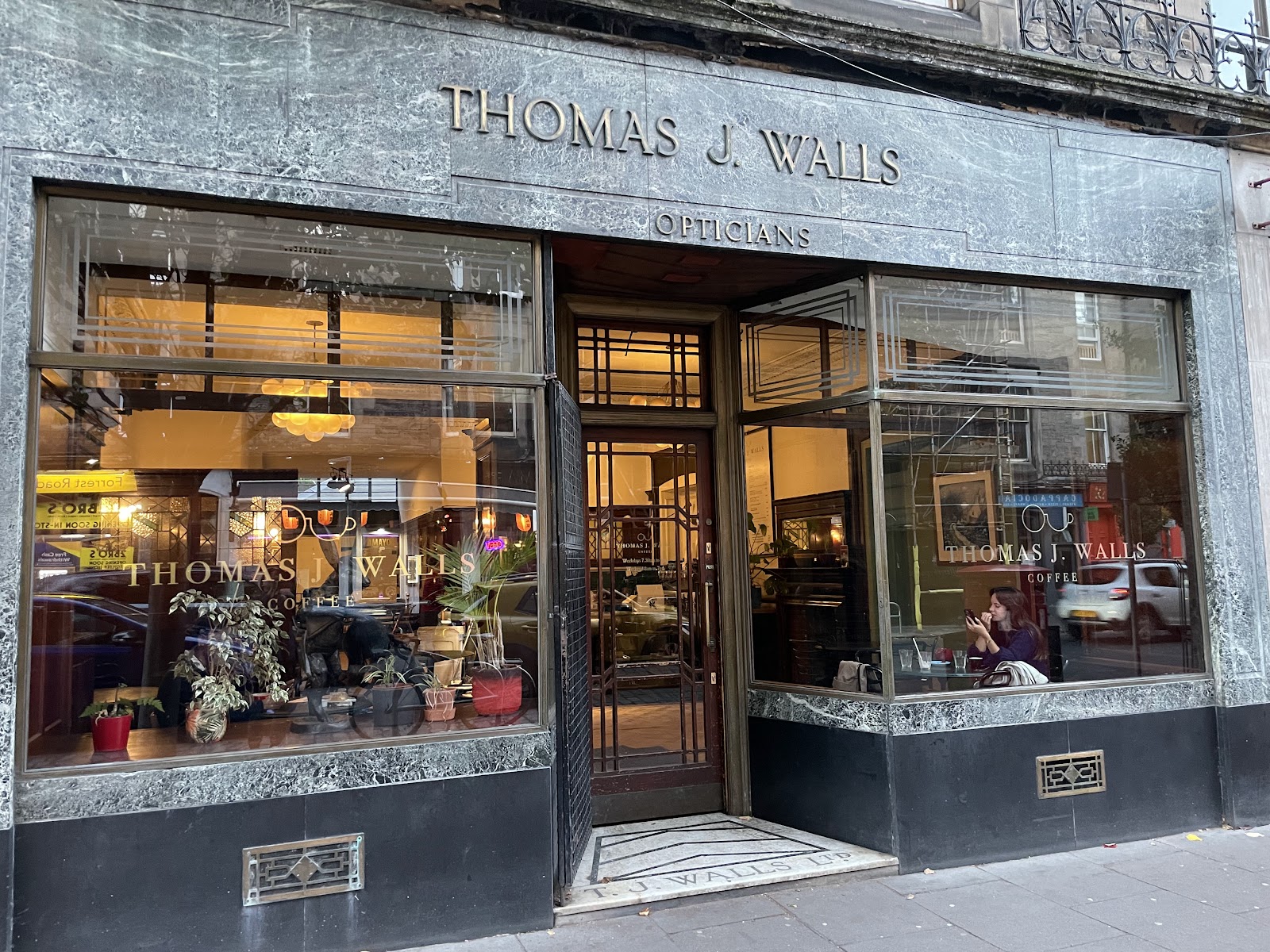 The marble shopfront of Thomas J Walls on Forrest Road, its old opticians' lettering above wide windows and a bronze door.